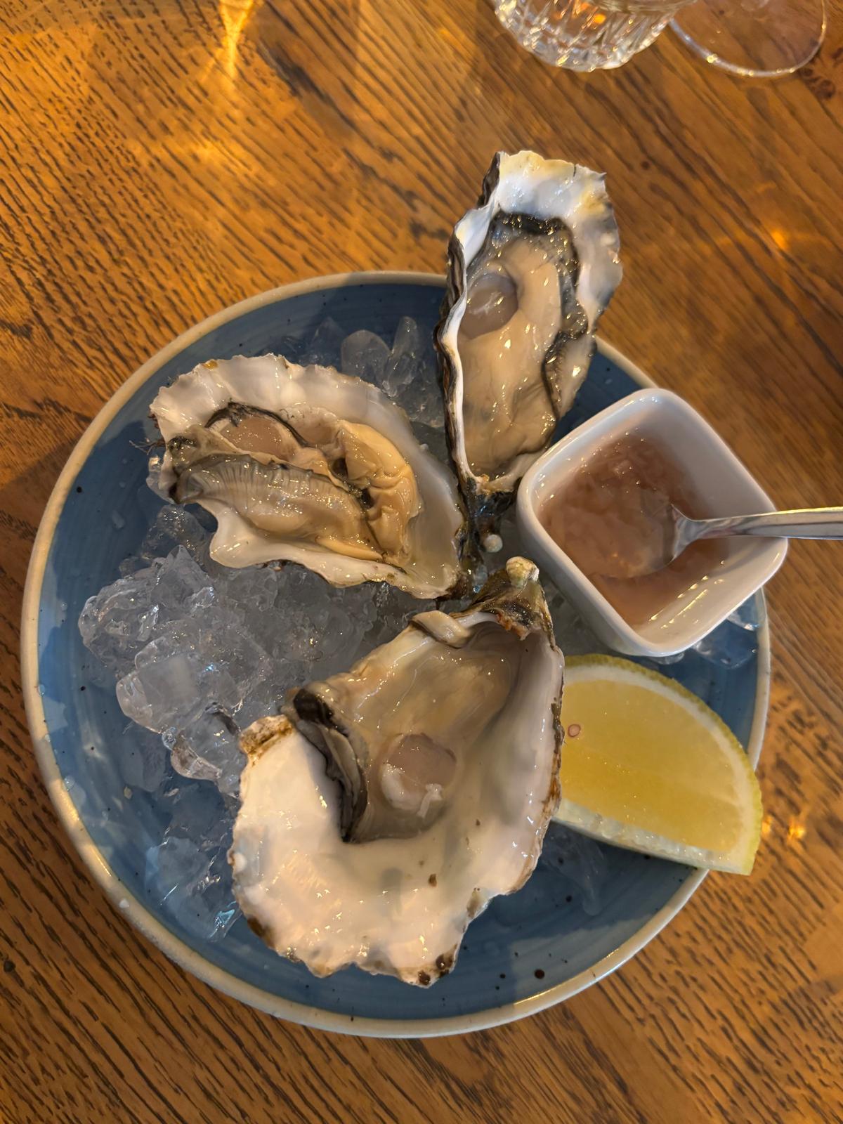 Bord met drie verse oesters op ijs, een schaaltje dressing en een partje citroen