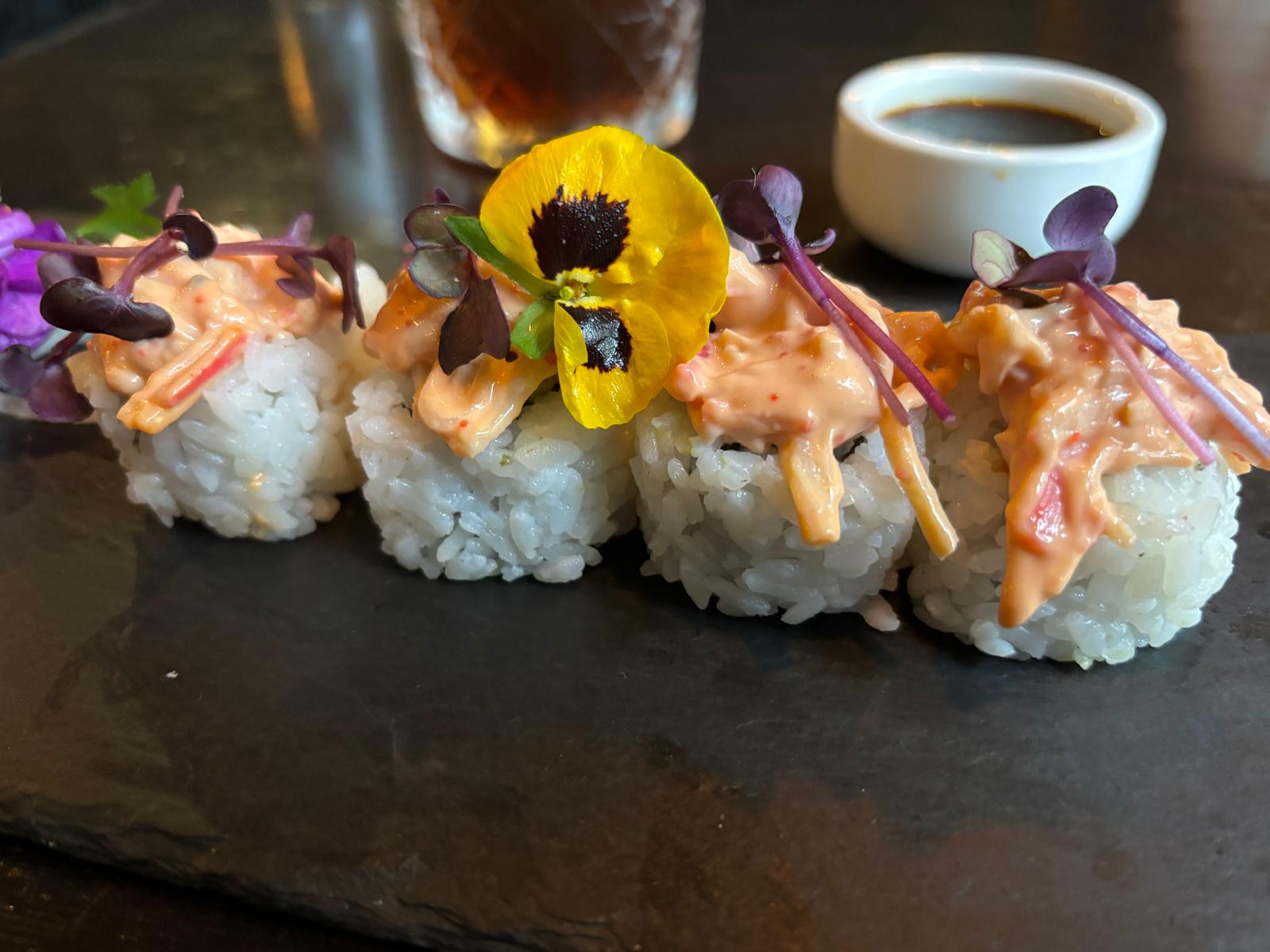 Vier sushirollen met romige topping, paarse kiemen en een gele eetbare bloem