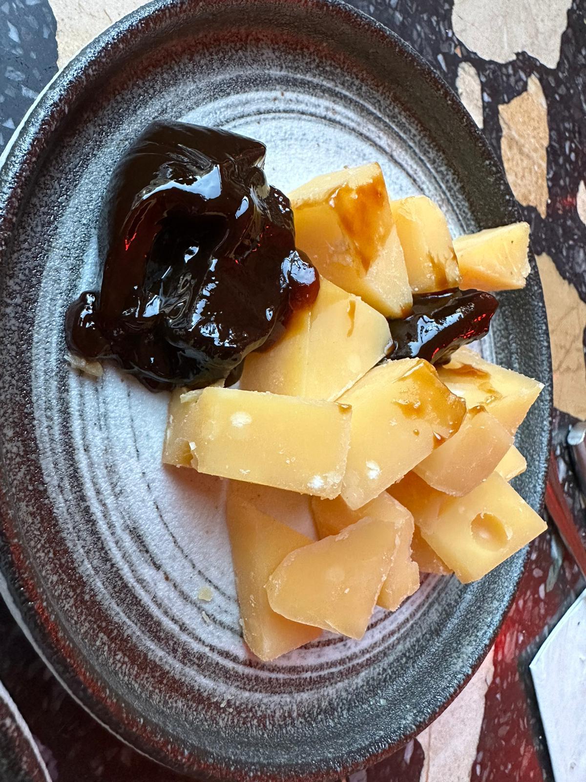 Blokjes kaas met een donkere chutney op een aardewerken bord
