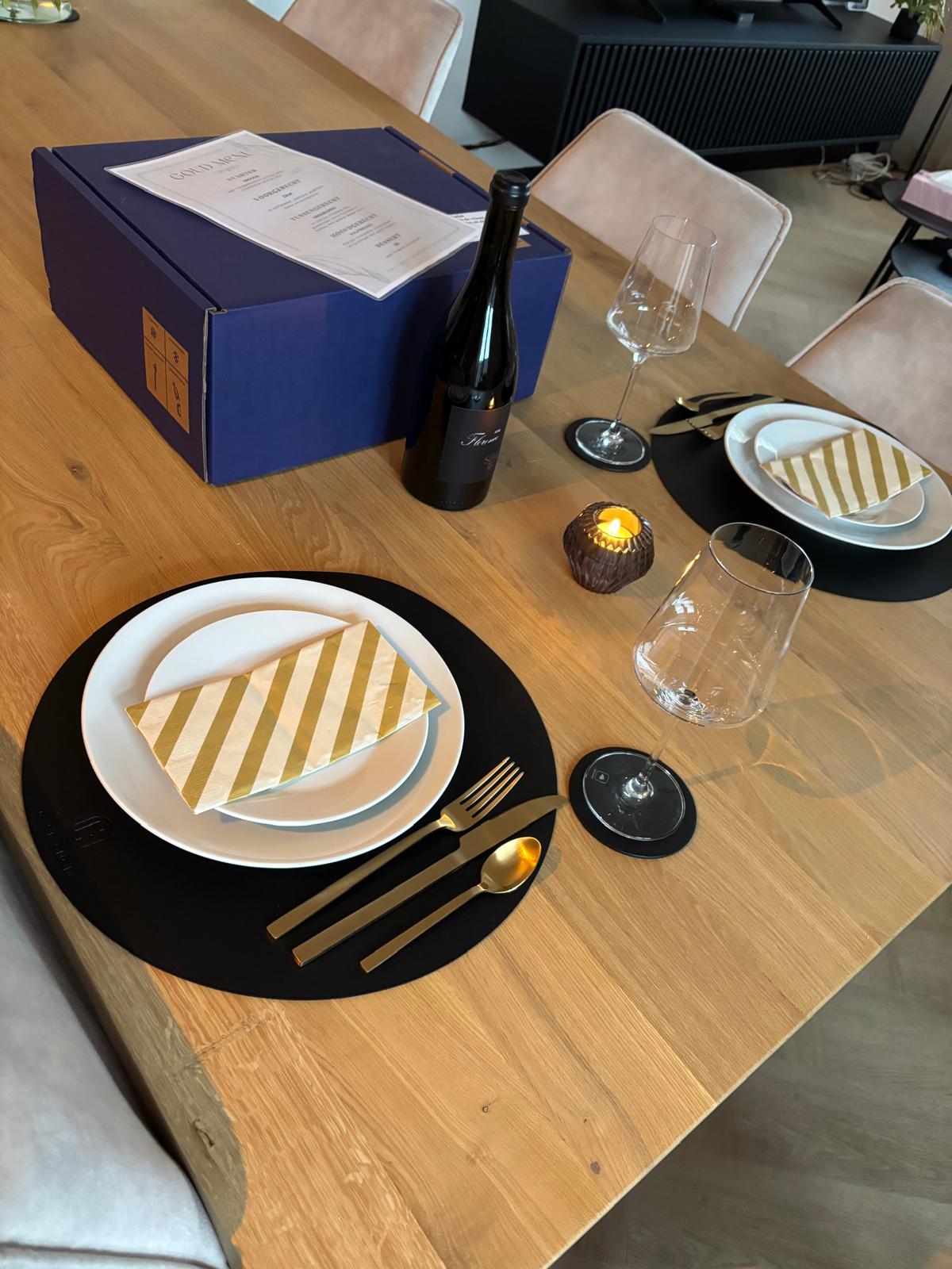 Gedekte eettafel met gouden bestek, kaars, wijnglazen, de blauwe SOUS doos en een fles Florence