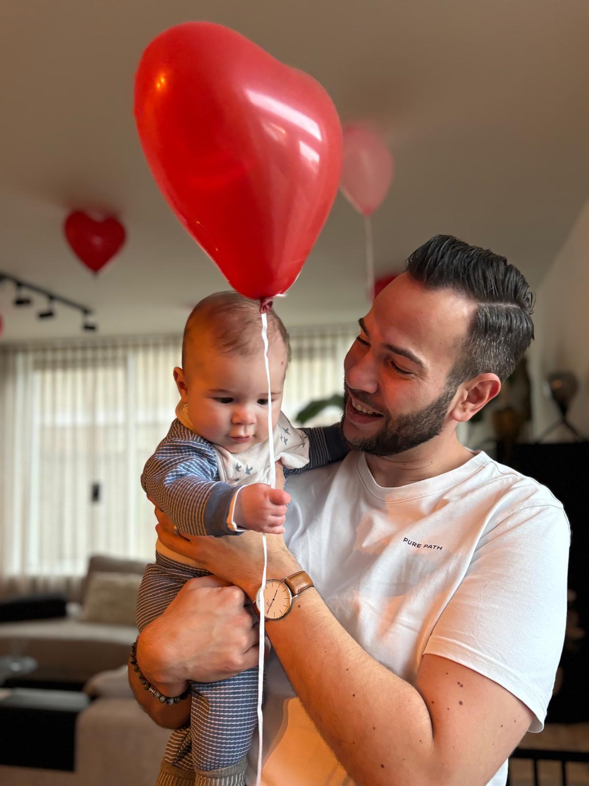 Sven met Mason op de arm en een rode hartjesballon in de woonkamer