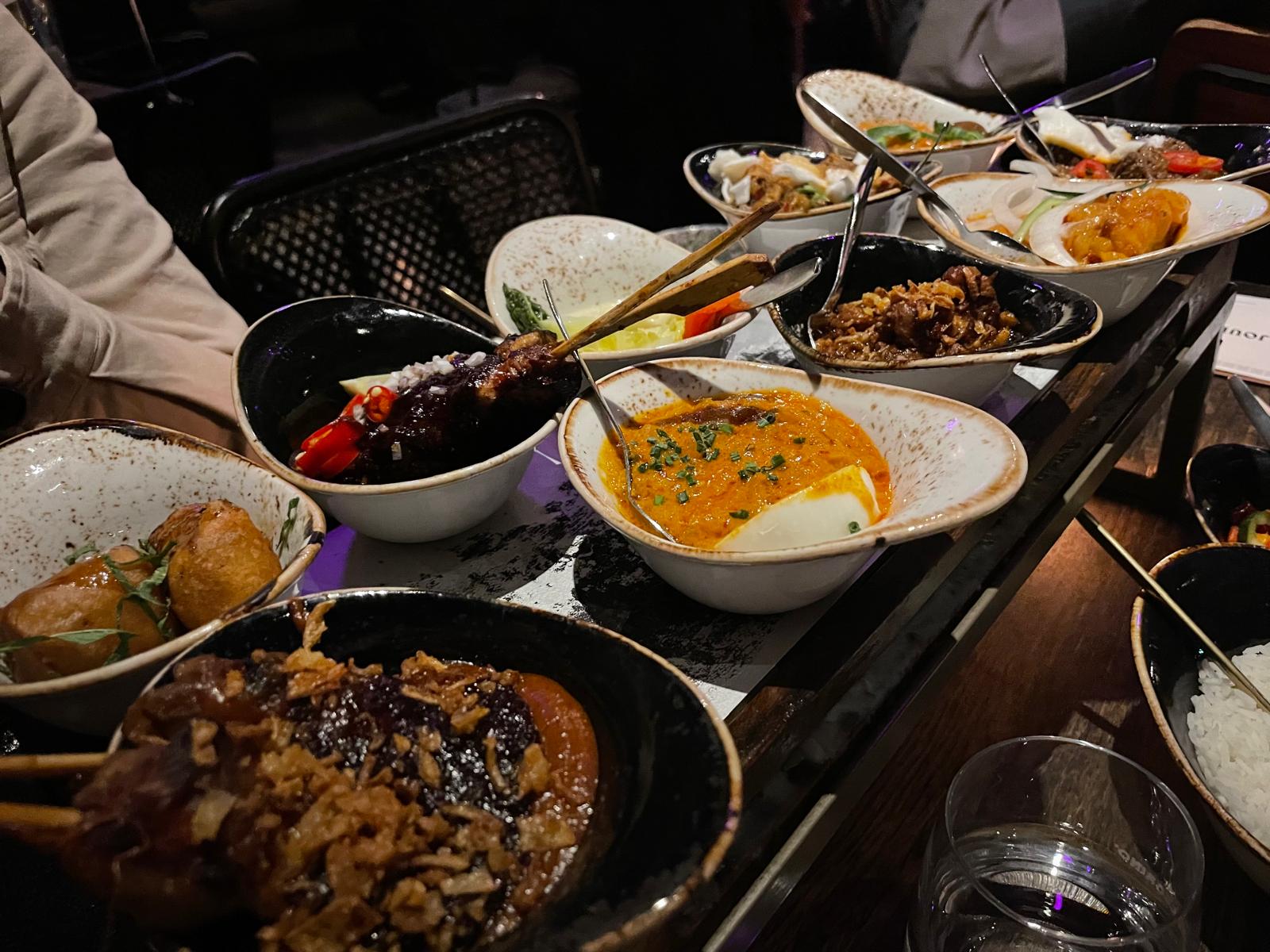 Een volle rijsttafel met kommen vol saté, curry, groenten en krokante hapjes