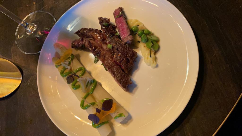 Rib-eye met witte asperge, doperwten en aardappelpuree op een wit bord
