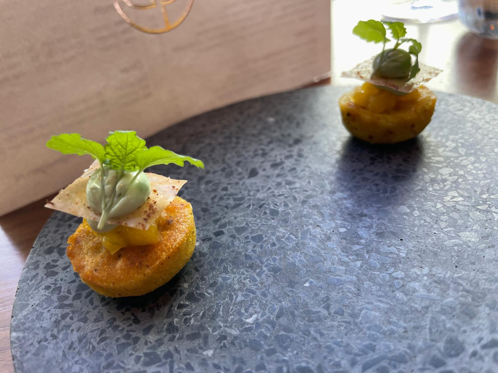 Twee kleine amuses met mango en kruiden op een stenen plateau