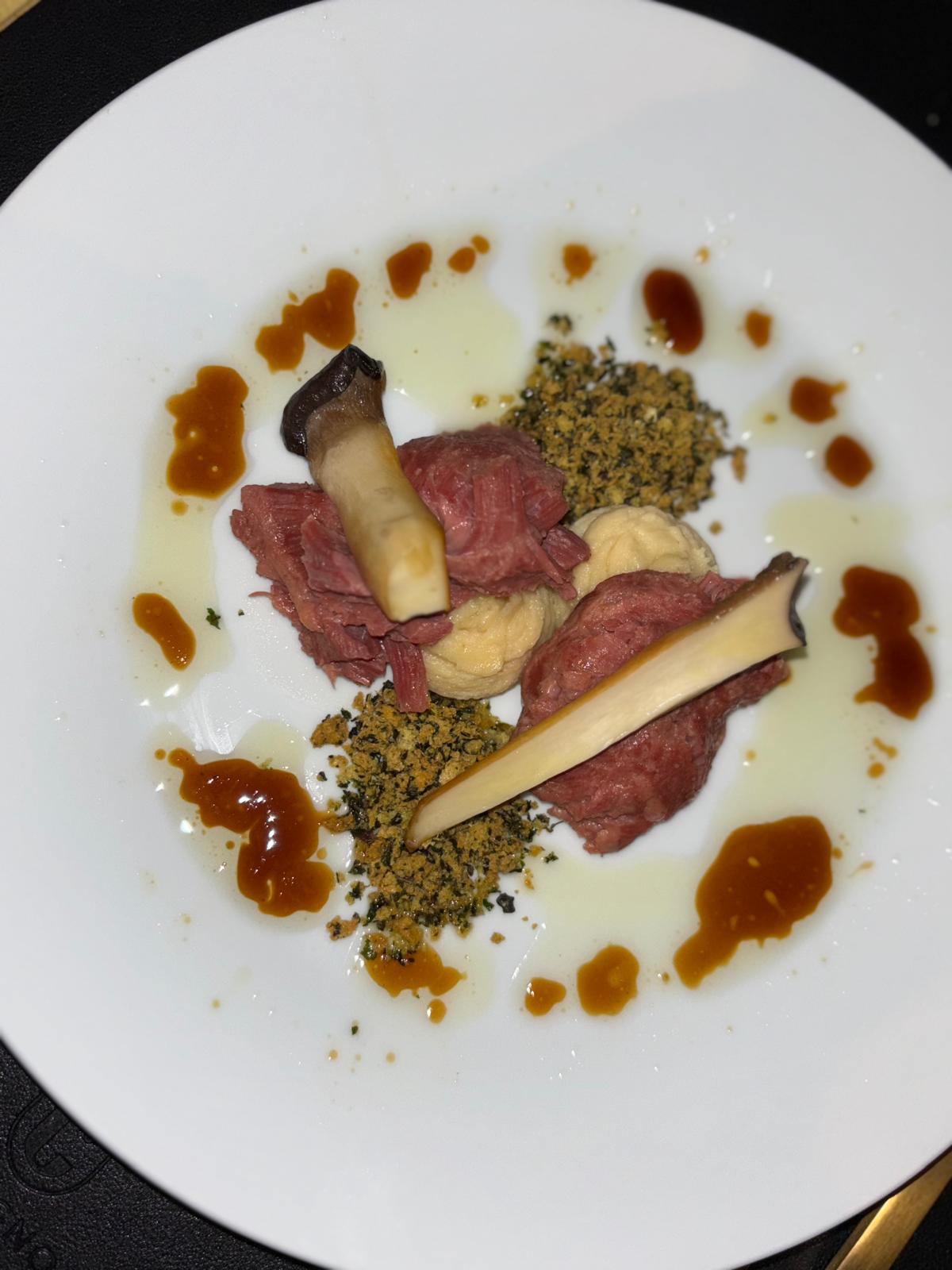 Rosé gebakken vlees met oesterzwam, crumble en jusdruppels op een wit bord