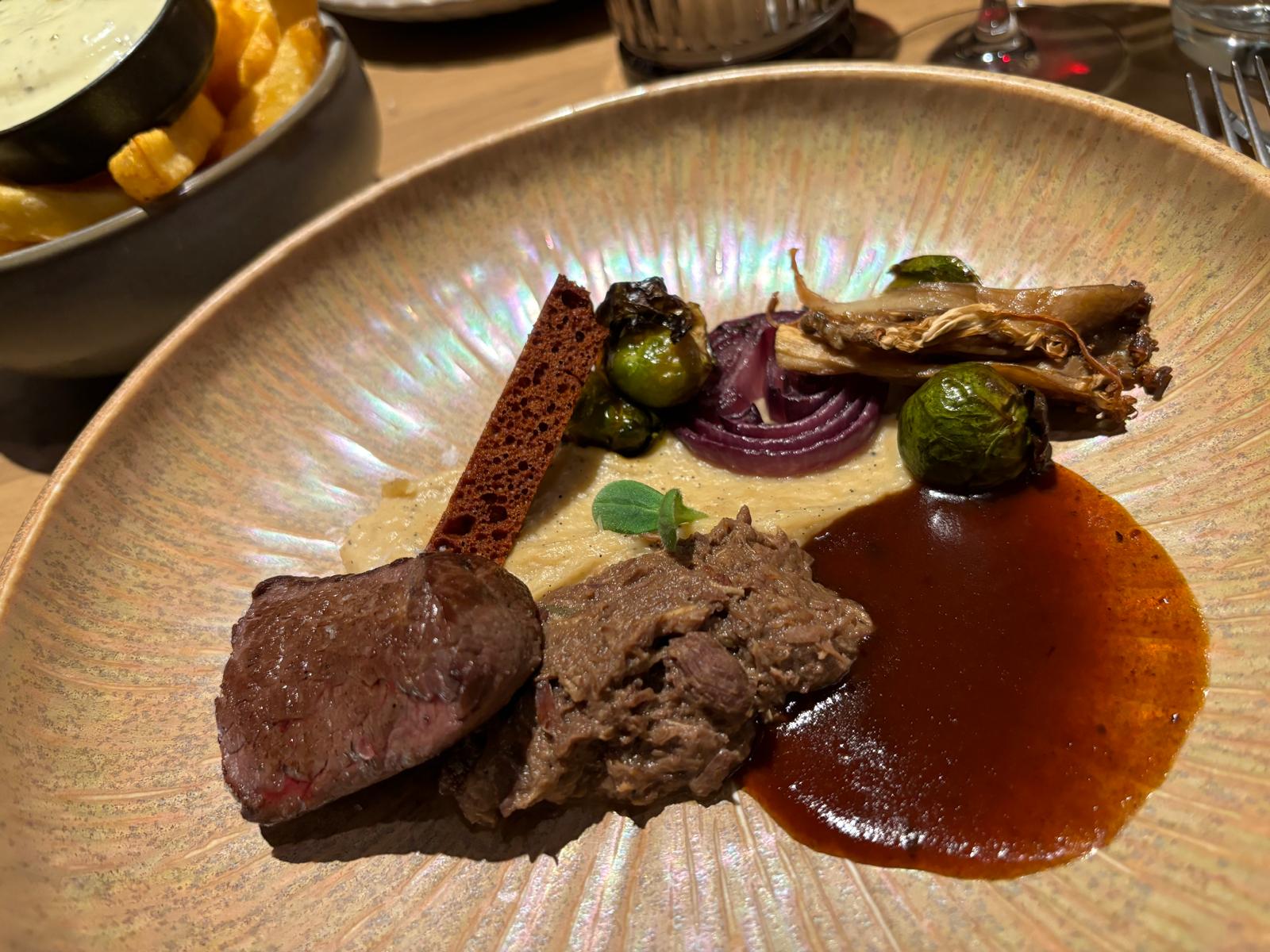 Gerecht met kort gebakken vlees, gestoofd rundvlees, spruitjes en een krachtige jus op een parelmoerkleurig bord