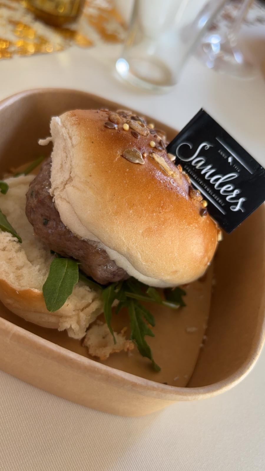 Klein broodje met een gegrilde burger en rucola in een kartonnen bakje