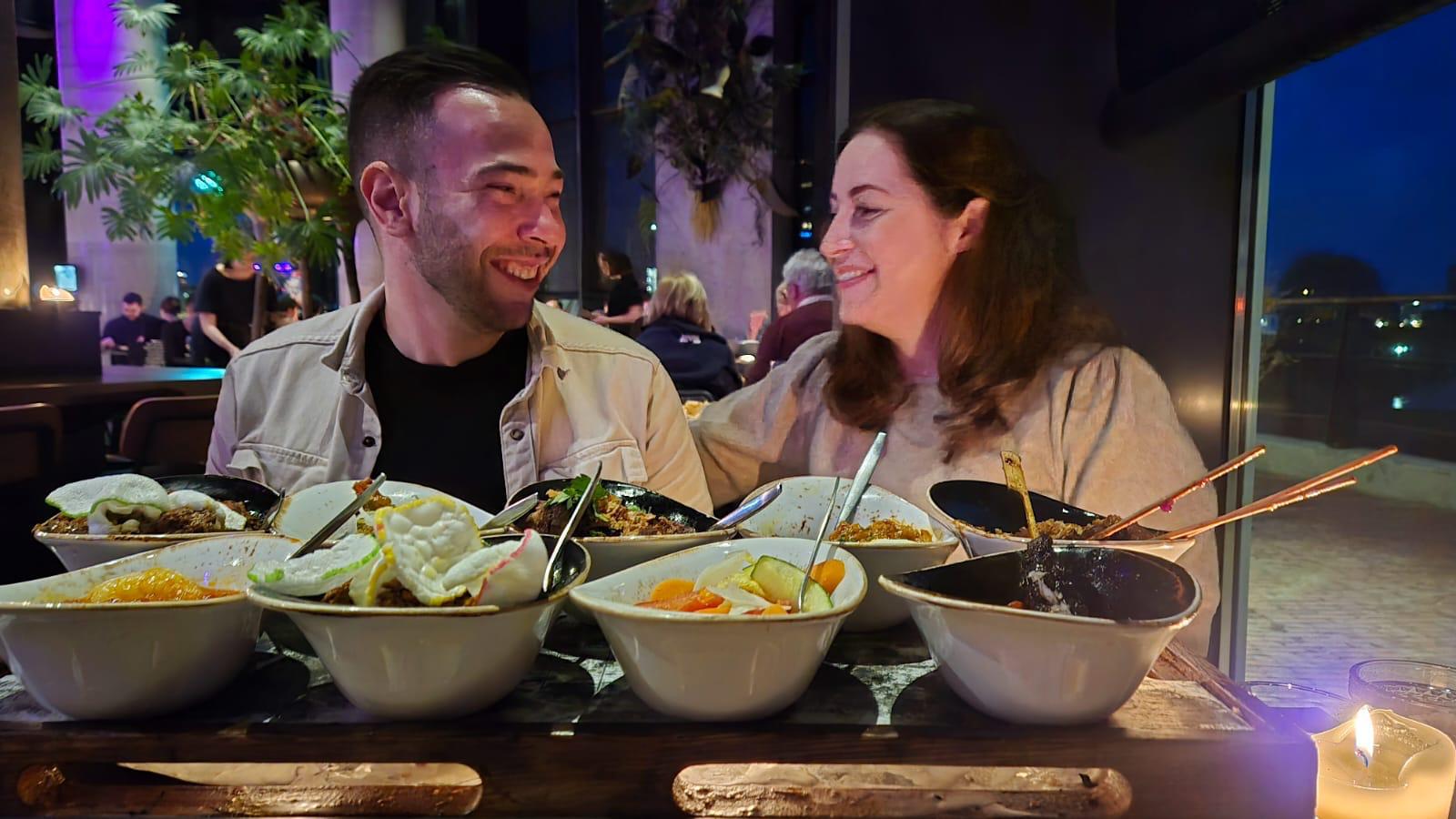 Sven en Eva lachend achter een volle tafel met Indische en Aziatische gerechten bij Bistrobar Bankoh