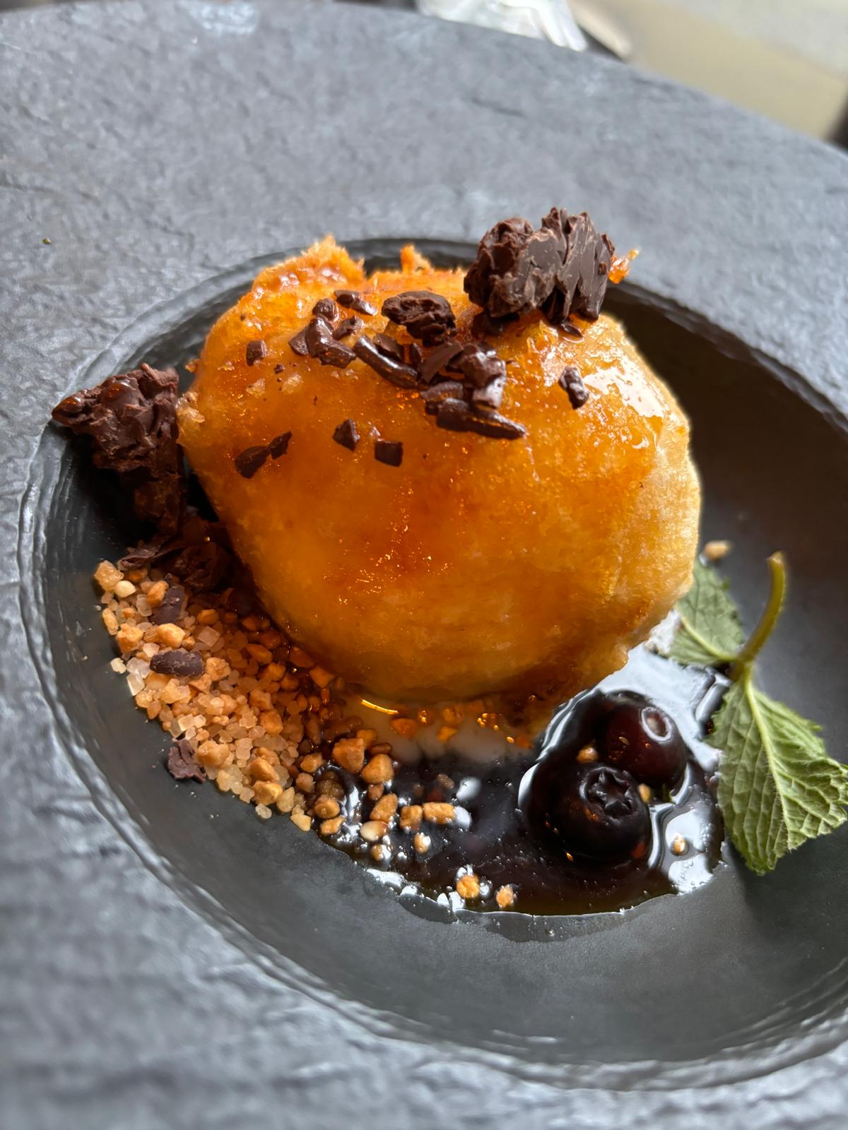 Warm dessert met krokante bol, chocolade, kersen en munt op een leisteen bord