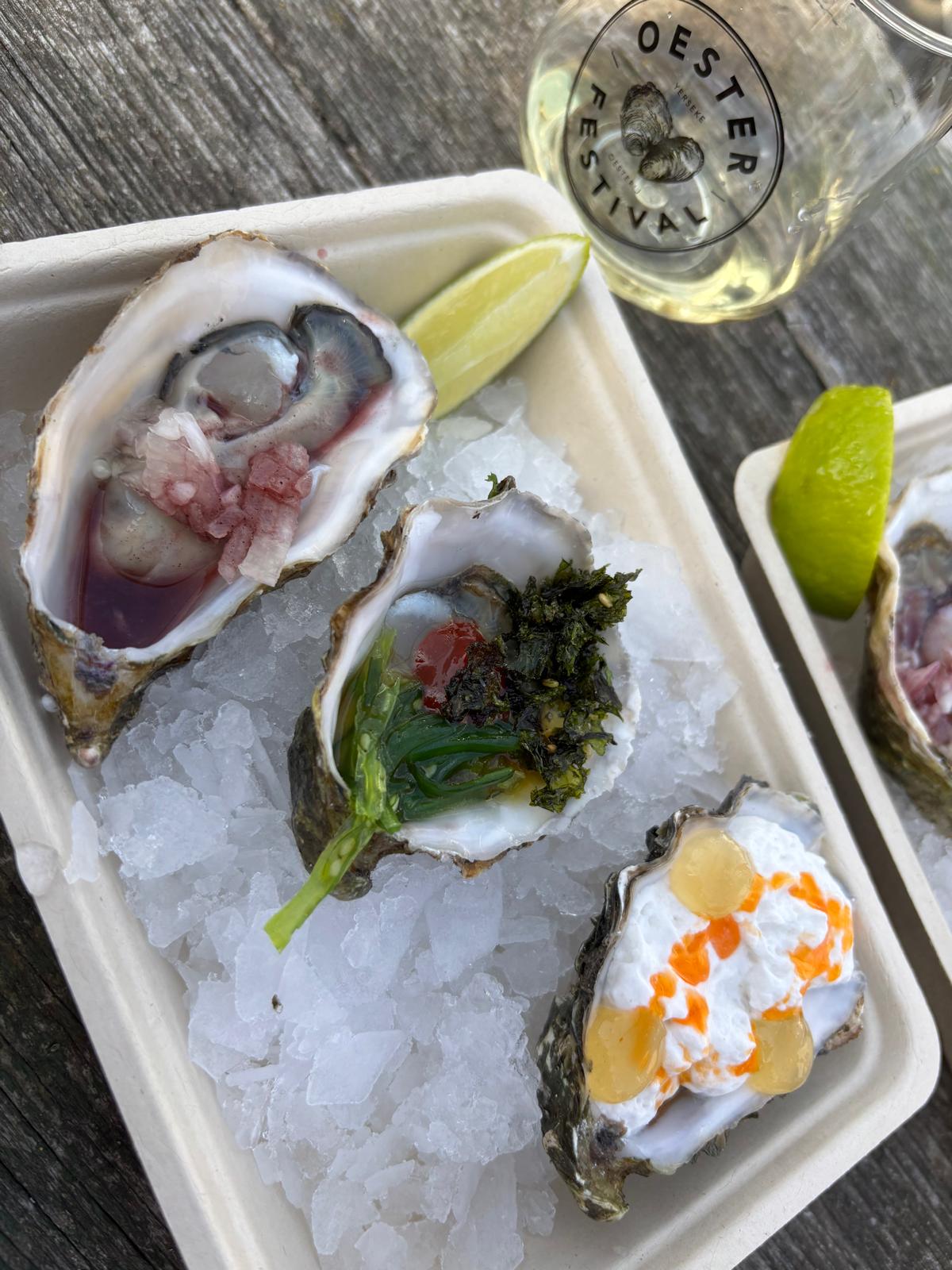 Oesters met verrassende toppings op ijs, naast een glas witte wijn met het beeldmerk van het Oesterfestival