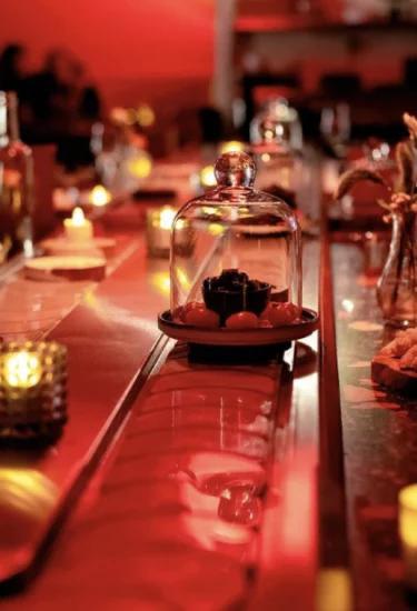 Warm rood verlichte bar met kaarsjes en een glazen stolp met een kleine kaasgerecht