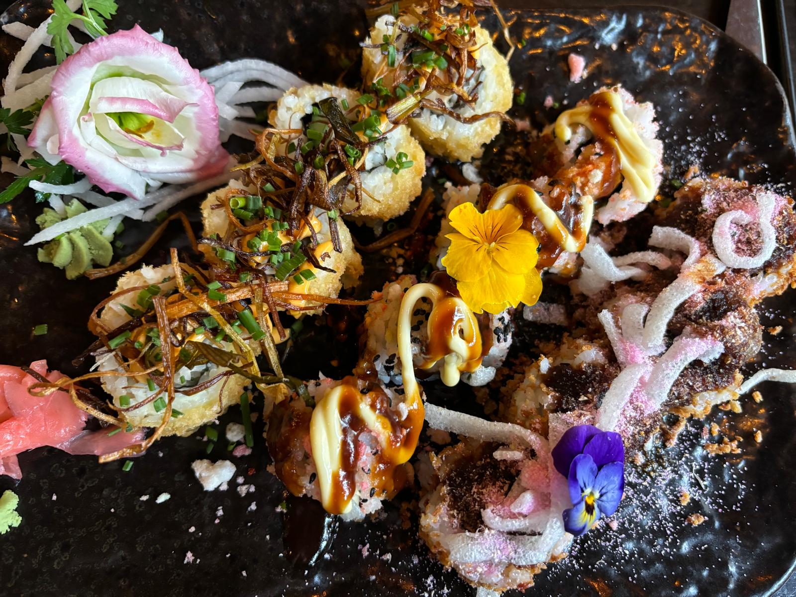 Kleurrijke sushirollen met eetbare bloemen en krokante toppings op een donker bord